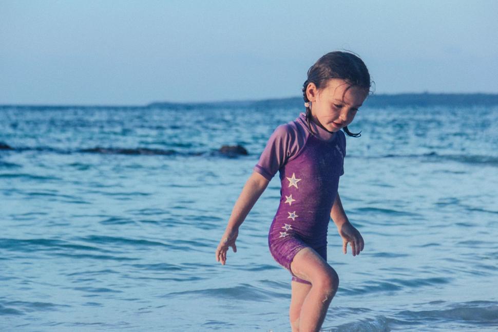 Free Image of Little Girl Standing on Surfboard in Ocean 