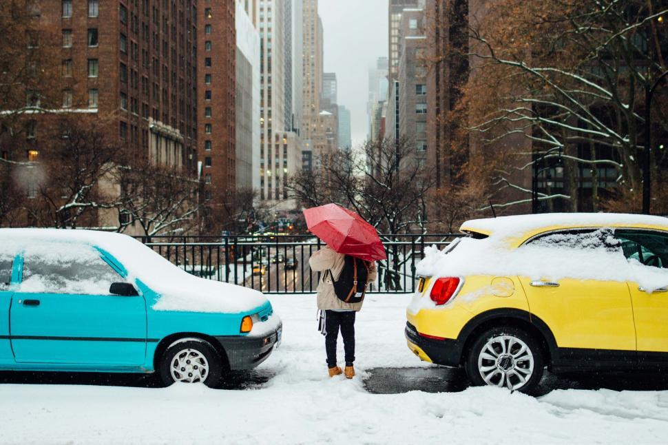 Free Image of Person With Umbrella Standing in Snow Next to Two Cars 