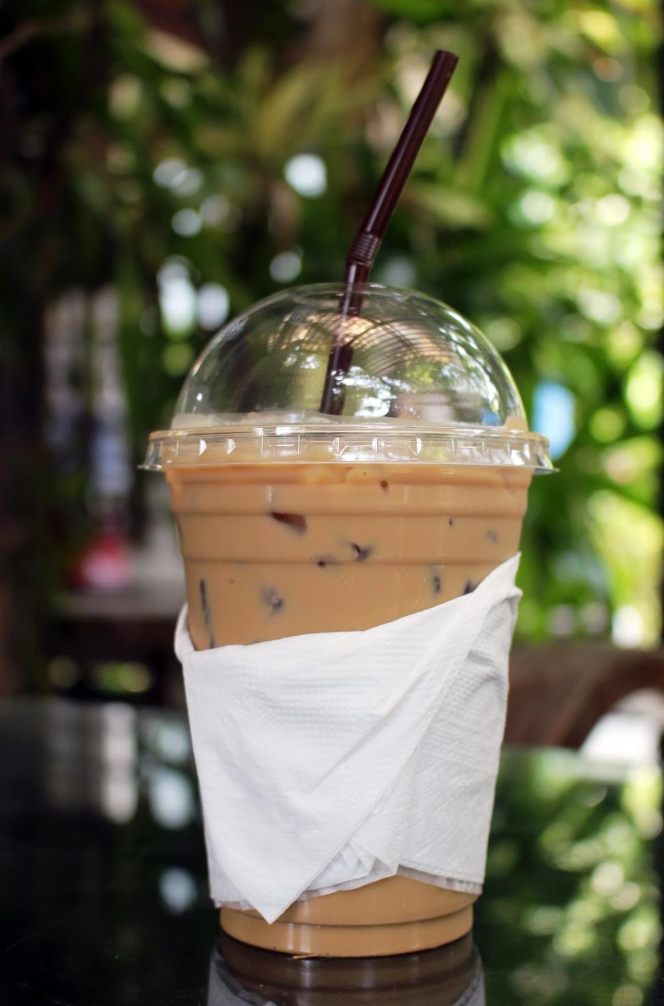 Free Image of Cup of iced coffee outside on a table in a tropical garden  