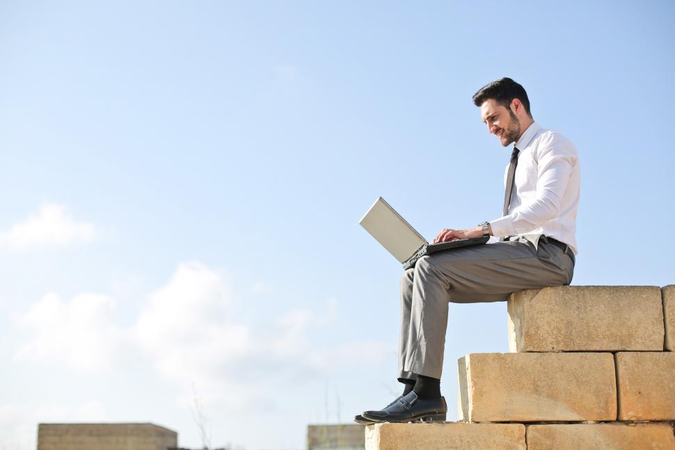 Free Image of Young Adult Man sitting on basalt bricks wall in formal clothing 
