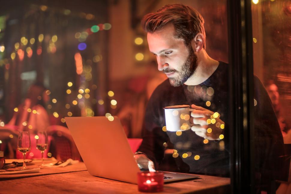Free Image of Young Adult Man Holding Mug in Front of Laptop 