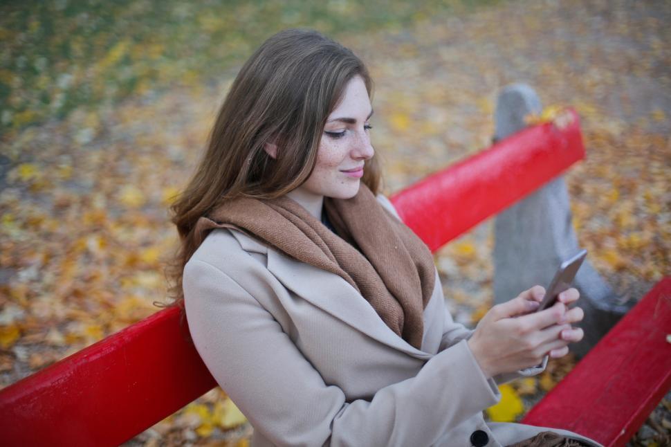 Free Image of Young Woman In Scarf And Beige Jacket Holding Cellphone While Si 