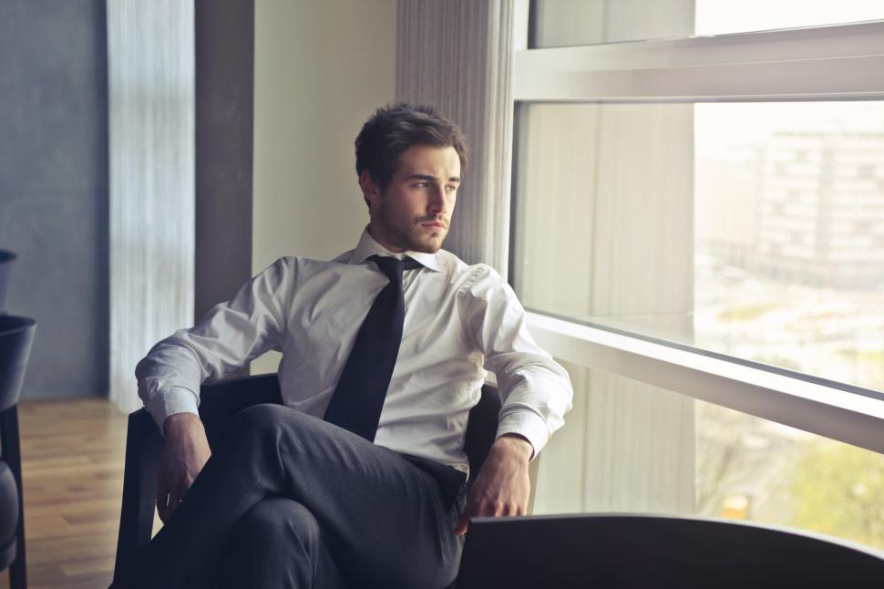 Free Image of Young man in white shirt and black tie sitting near window durin 