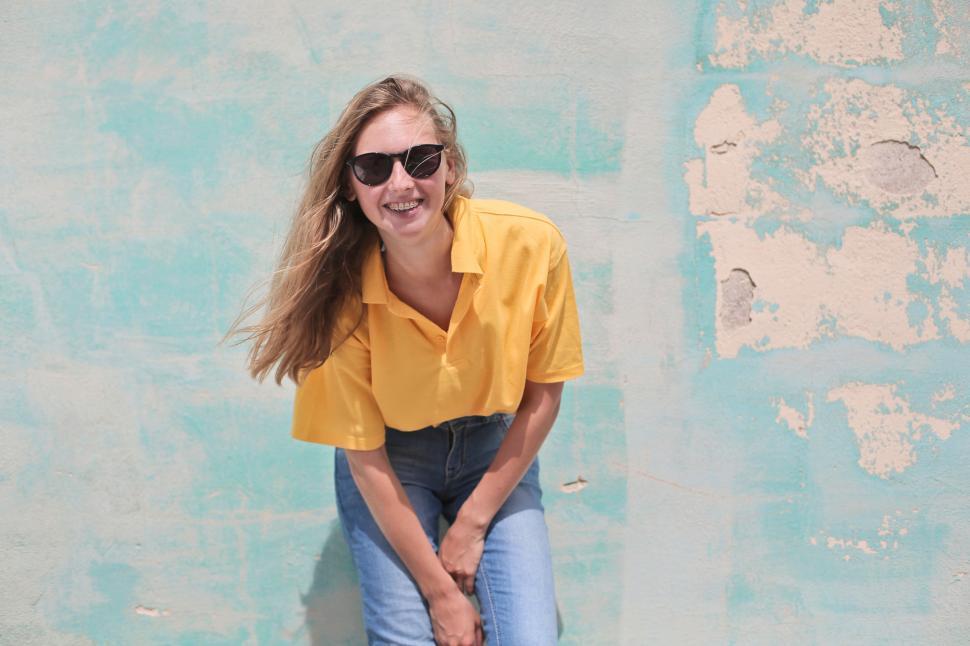 Free Image of Woman Wearing Yellow Polo Shirt Standing in Front of Teal Concre 