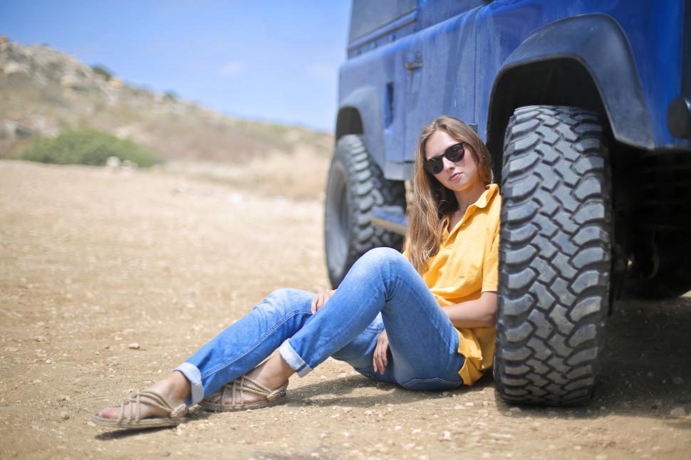 Free Image of Young Woman In Yellow Polo Shirt Sitting Besides SUV Tyre  In Th 