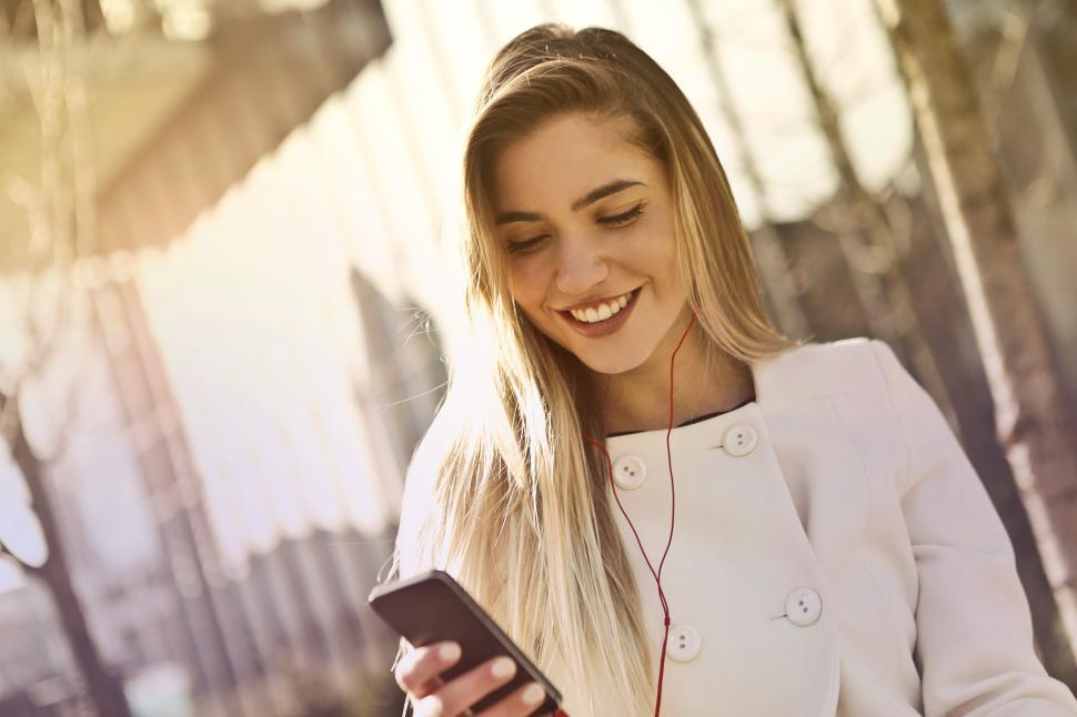 Free Image of Young Blonde Woman Wearing White Top Holding Smartphone And List 