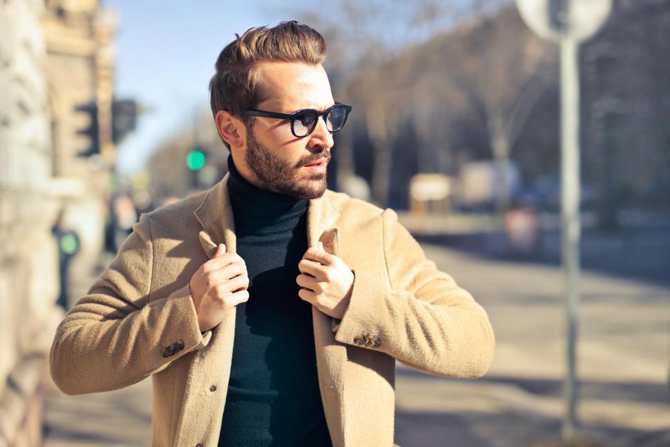 Free Image of Young Adult Man wearing beige jacket and sunglasses posing on th 