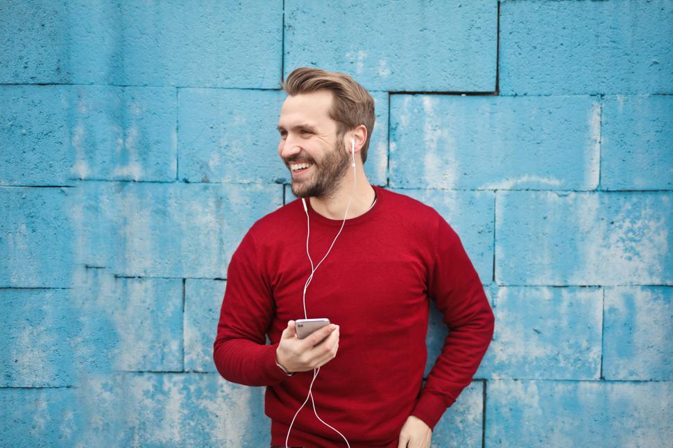 Free Image of Young man listening to music in his cellphone against turquoise 