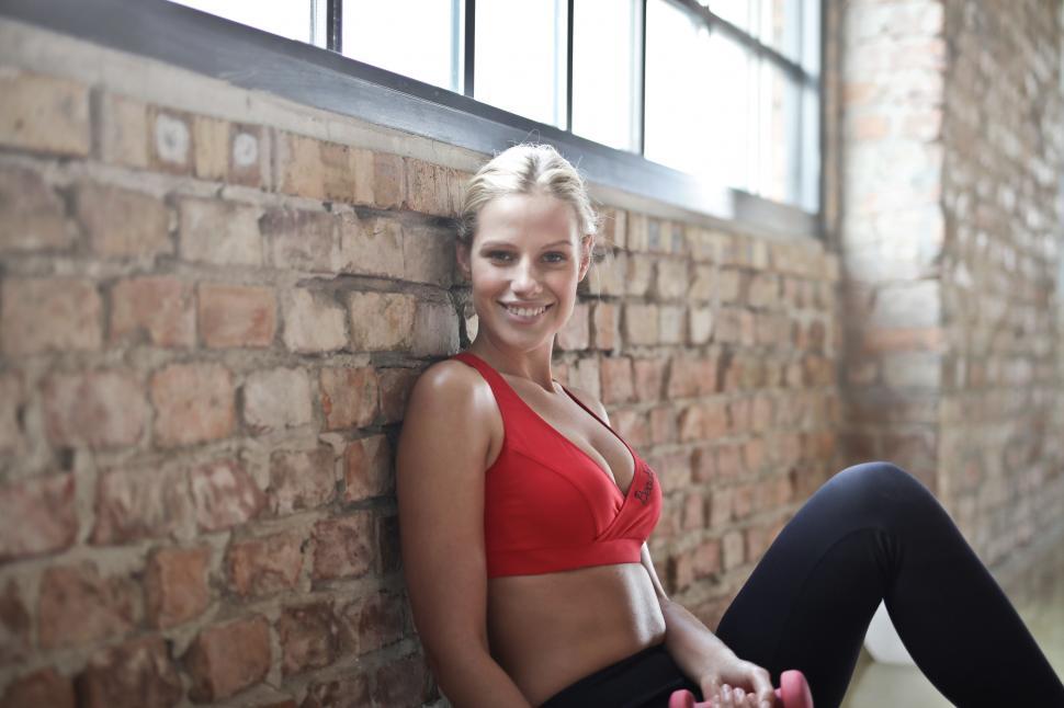 Free Image of Young Woman Wearing Red Sports Bra Sitting Against Brown Brick W 