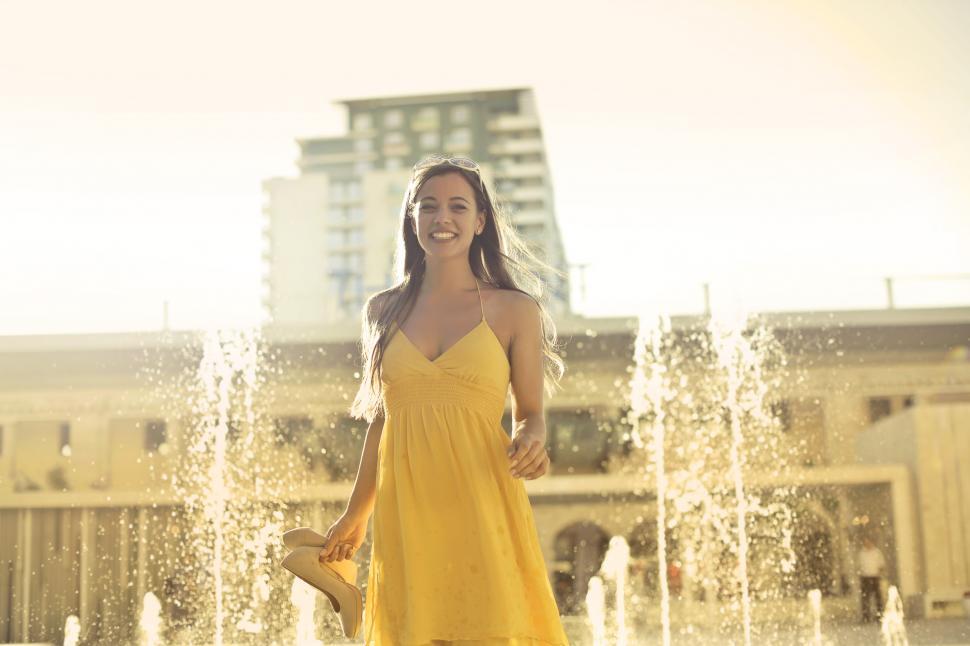 Free Image of Young Woman In Yellow Spaghetti Strap Dress Stands Near Water Fo 