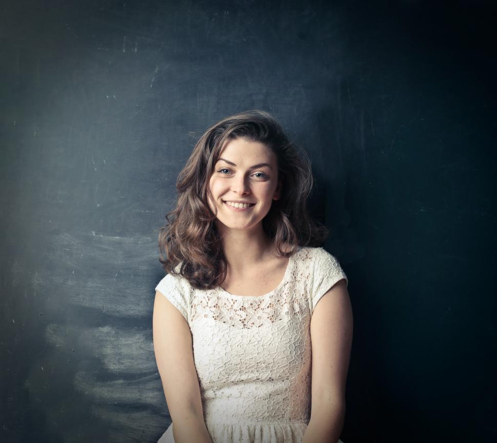 Free Image of Brown Haired Woman Smiling While Standing Against Blackboard 