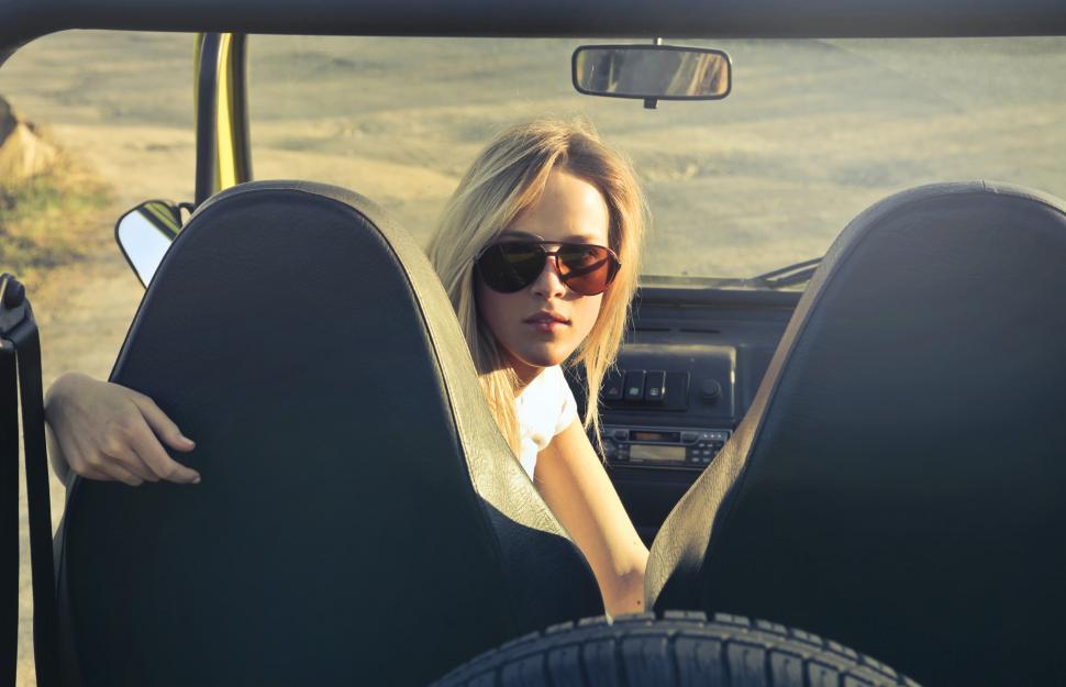 Free Image of Young woman in sunglasses sitting on the passenger seat of the c 