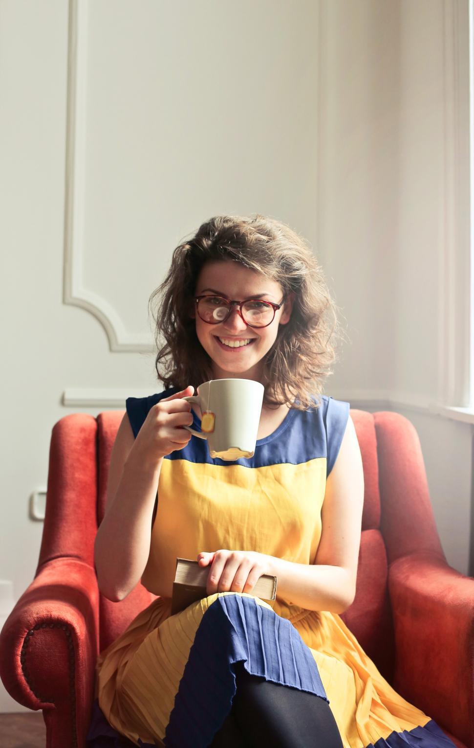 Free Image of Young Woman Sitting On Red Armchair While Enjoying A Cup Of Tea 