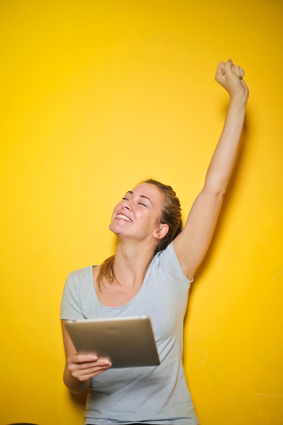 Free Image of Young Woman Holding An iPad With One Hand Up Against Yellow Wall 