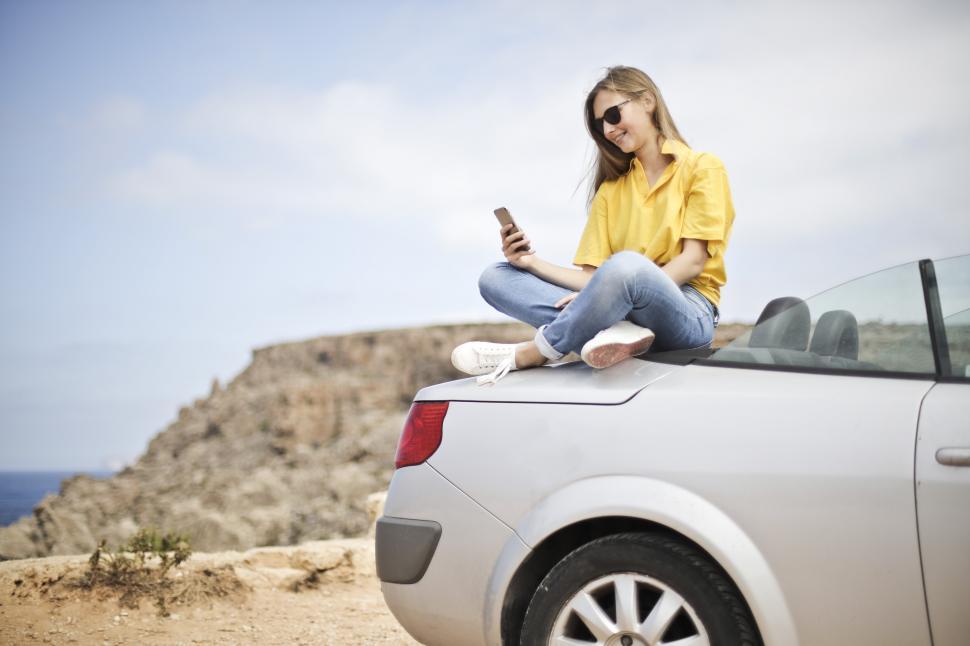 Free Image of Young Woman in Yellow Shirt and Denim Jeans Using Smartphone on 
