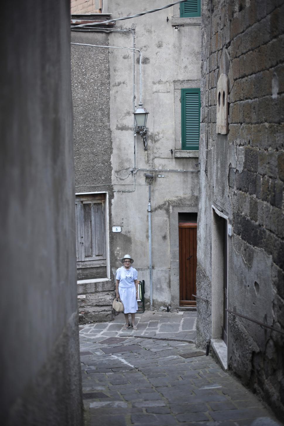 Free Image of Elderly Woman Walking On Cobblestone Street 