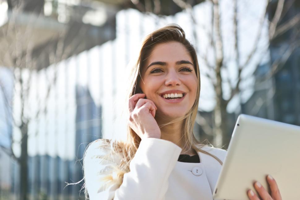Free Image of Young Woman In White Jacket Smiling While Using Smartphone And T 
