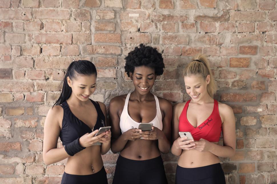 Download Free Stock Photo of Three multi ethnic women in sportswear looking at their mobiles. 