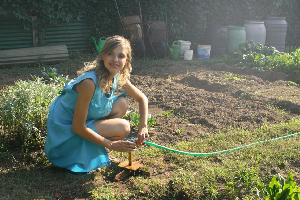 Free Image of A young blonde woman in shirt dress holding a plant watering fou 