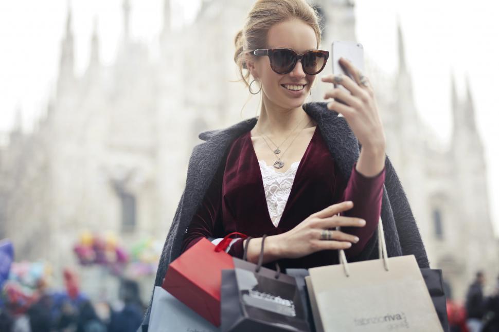 Free Image of A young blond woman looks at her mobile phone holding while shop 