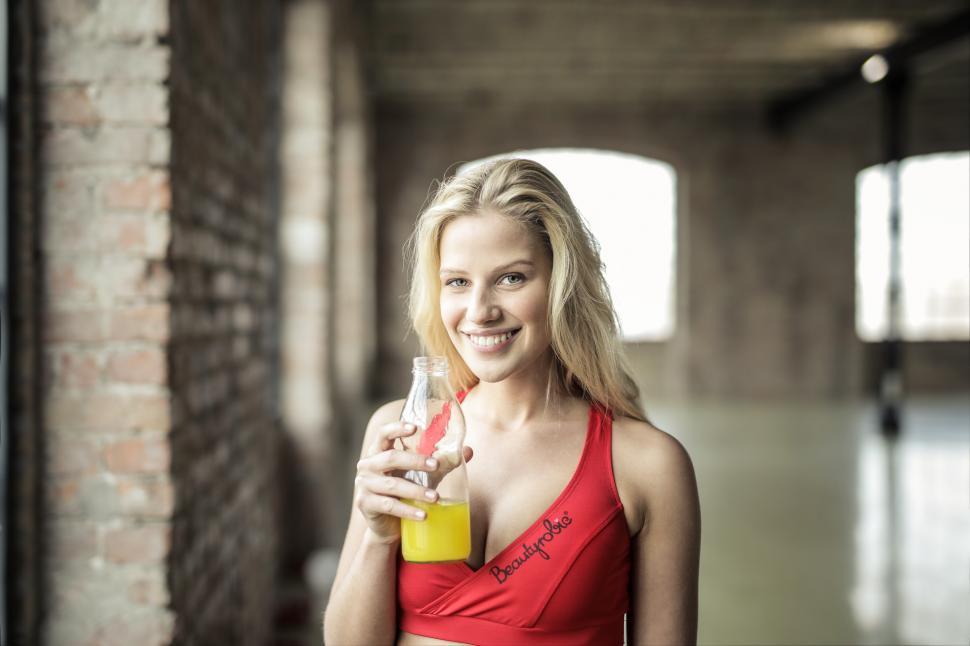 Free Image of A yound blonde woman posing with juice bottle in her hand 