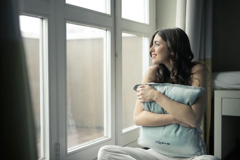 Free Image of A young brunette woman looks outside the window 
