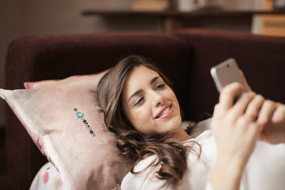 Free Image of A young woman  laying on the couch looking at her mobile phone 