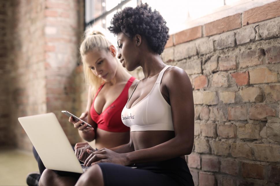 Free Image of Two multiethnic women wearing sports bra looking at mobilephone 