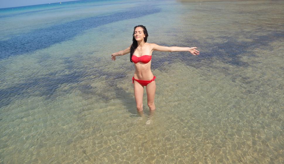 Free Image of Woman In Red Bikini Posing With Open Arms In Beach Water 