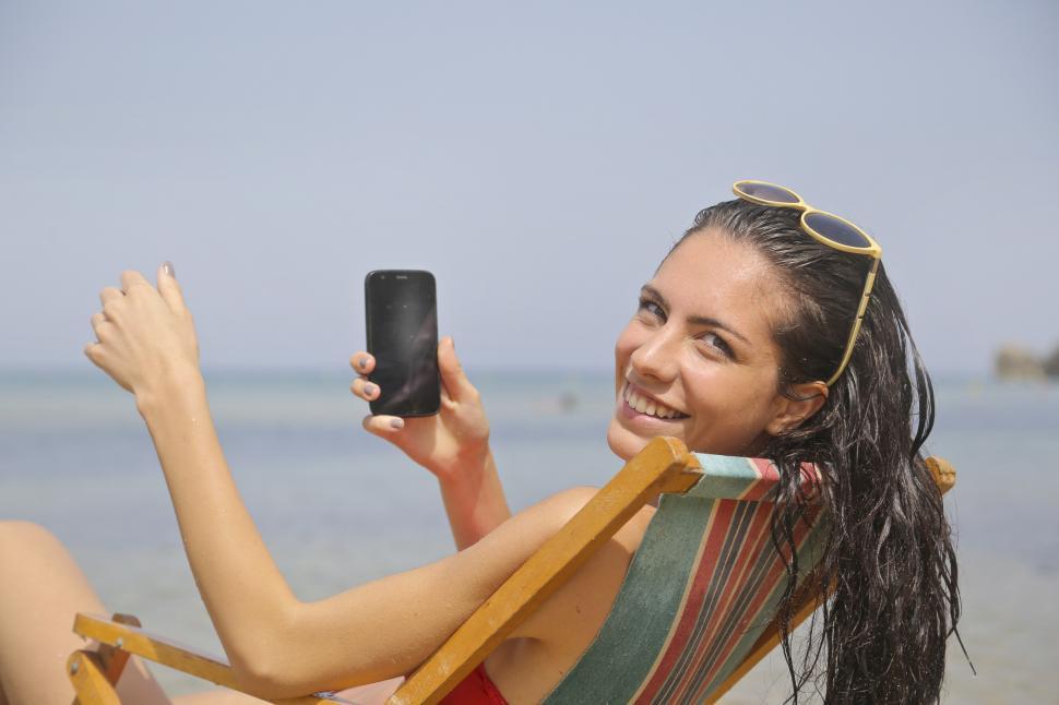 Free Image of Young Woman holding her phone while relaxing on beach chair 