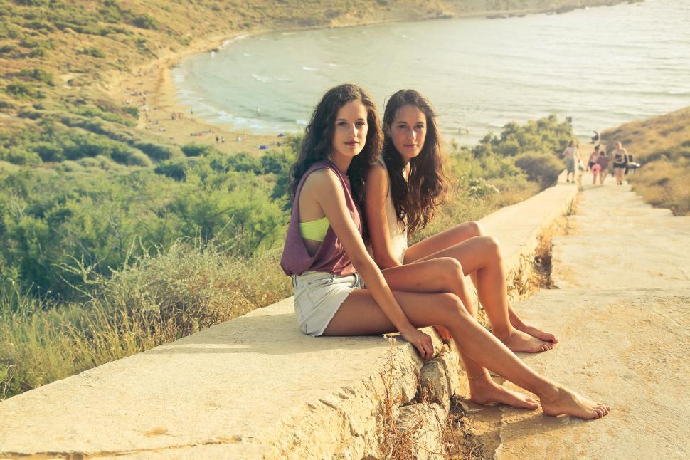 Free Image of Two young brunette women in casuals sitting on the near a beach 