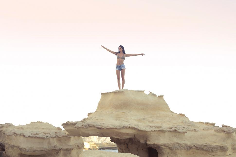 Free Image of A young brunette woman in bikini standing on a rock with her arm 