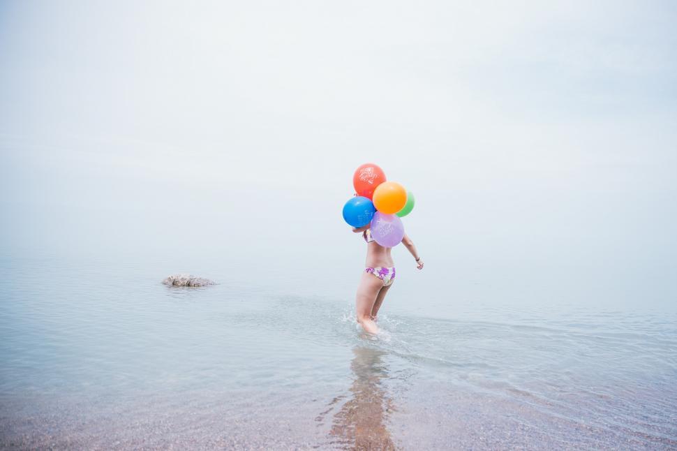 Free Image of A young caucasian woman in bikini holding balloons on the beach 