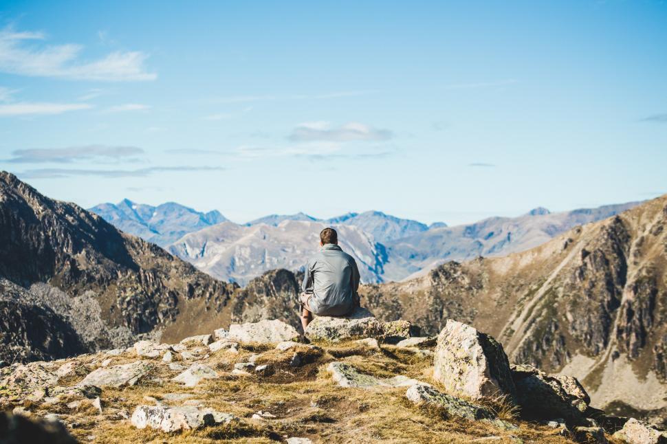 Free Image of A young traveler sitting on the edge of a cliff and watching the 