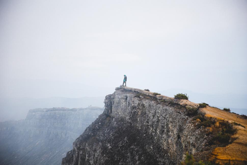 Free Image of A young hiker peaks over a rocky edge 