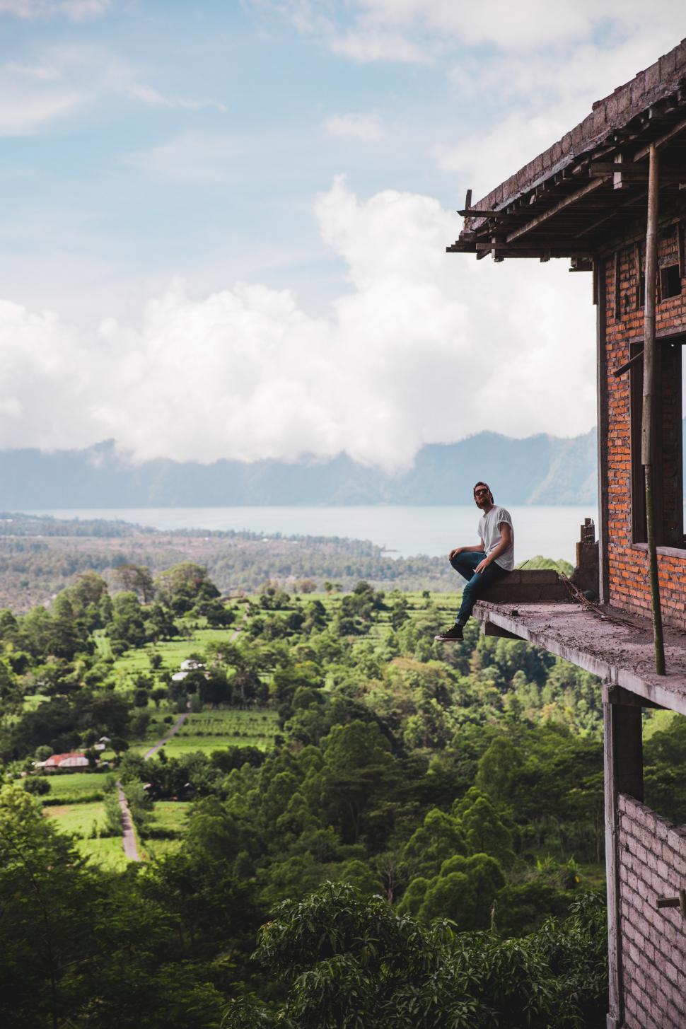 Free Image of A young Caucasian man sitting on the edge of a balcony 