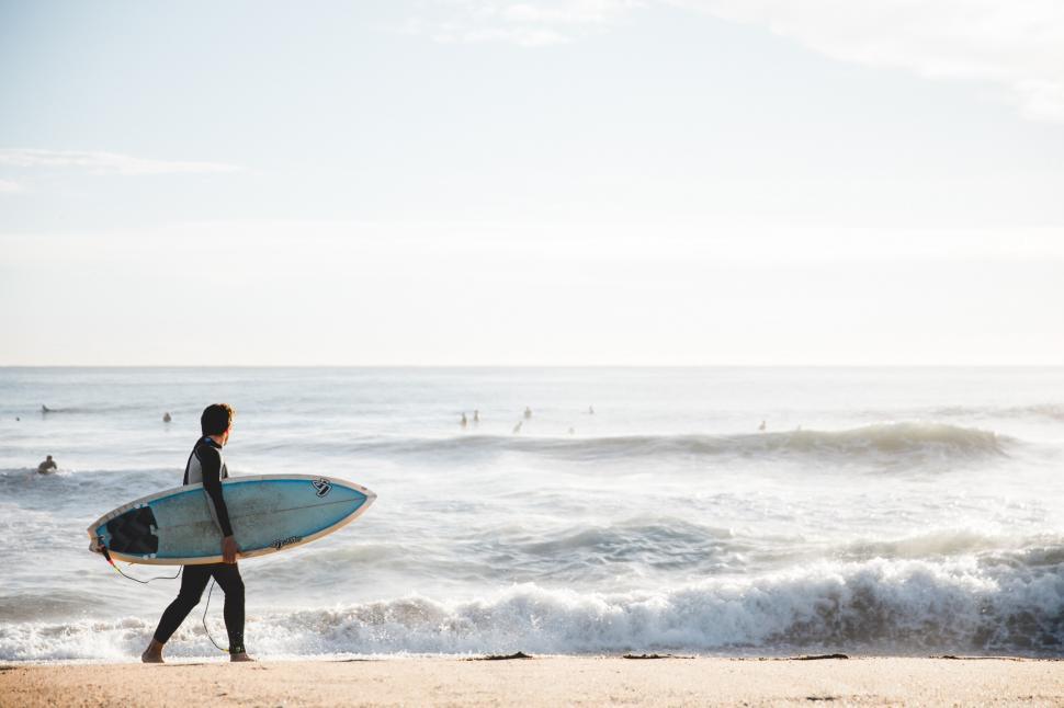 Free Image of A young Caucasian surfer carrying surfboard on the beach 