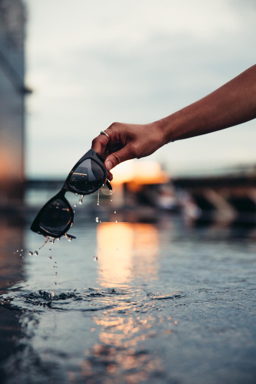 Free Image of Drenched sunglasses held with a hand over water 