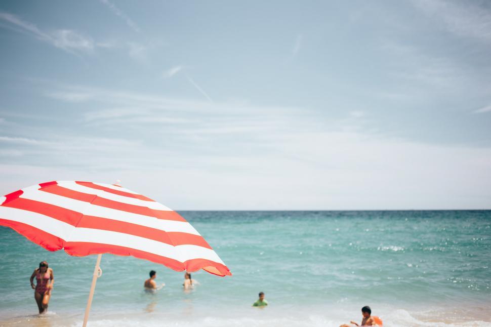 Free Image of A beach umbrella and people swimming 