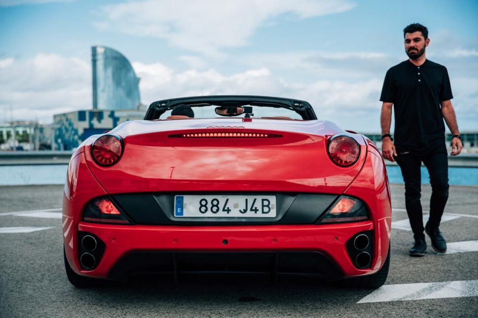 Free Image of A young man standing beside a red convertible sports car 