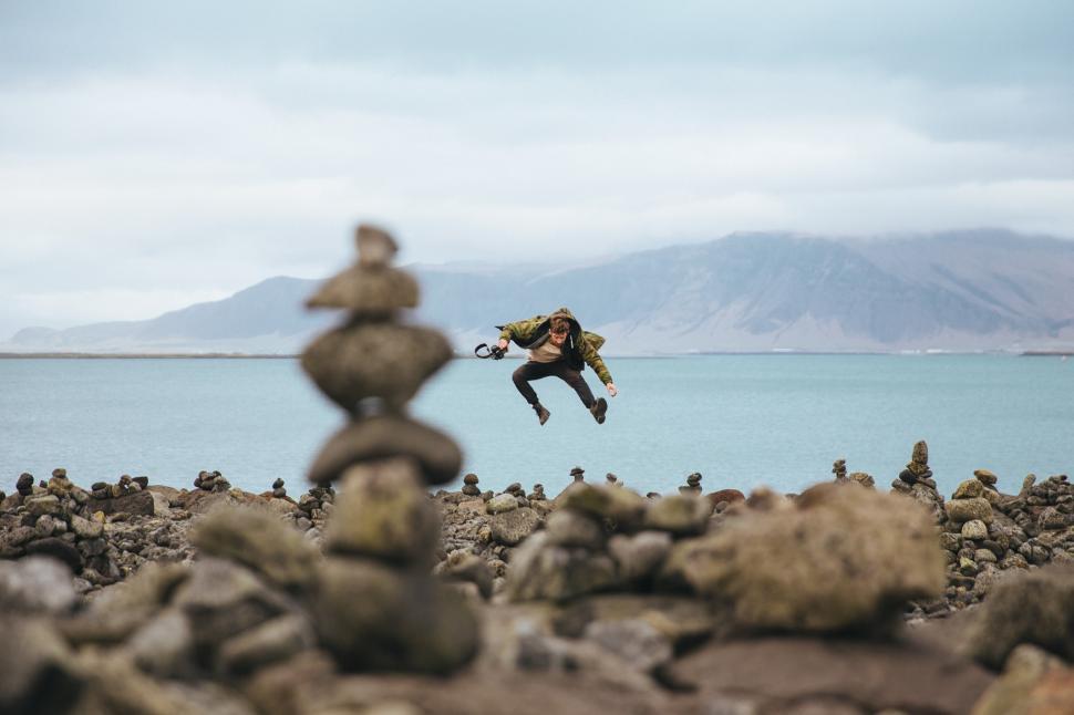 Free Image of A young caucasian hiker jumping on a stoney shore 