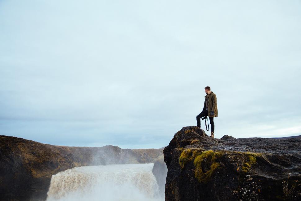 Free Image of A hiker on a cliff by the waterfall 