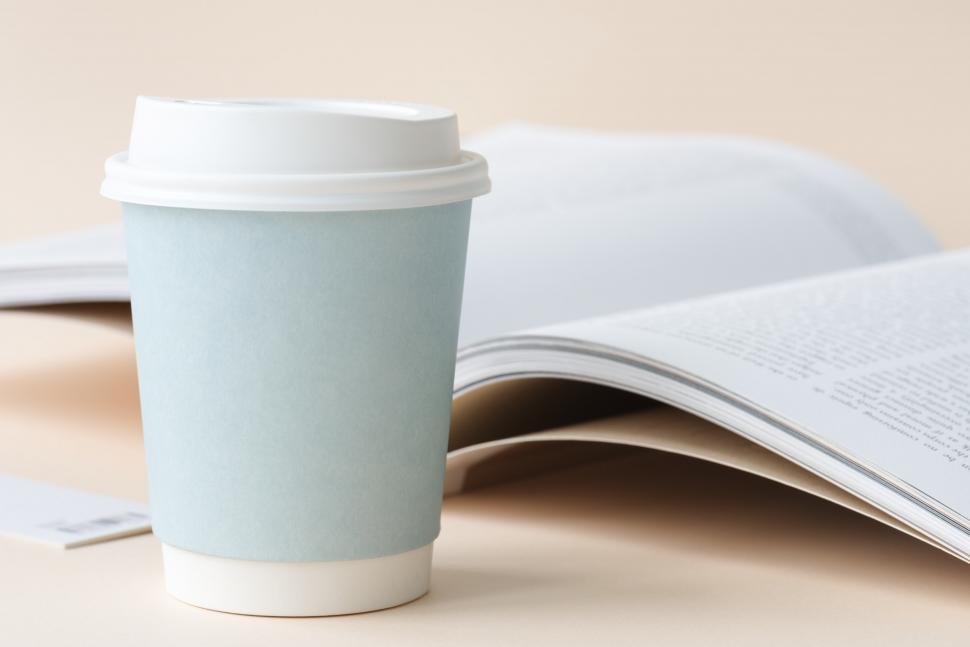 Free Image of Close up of a paper coffee cup with an open book in the backgrou 