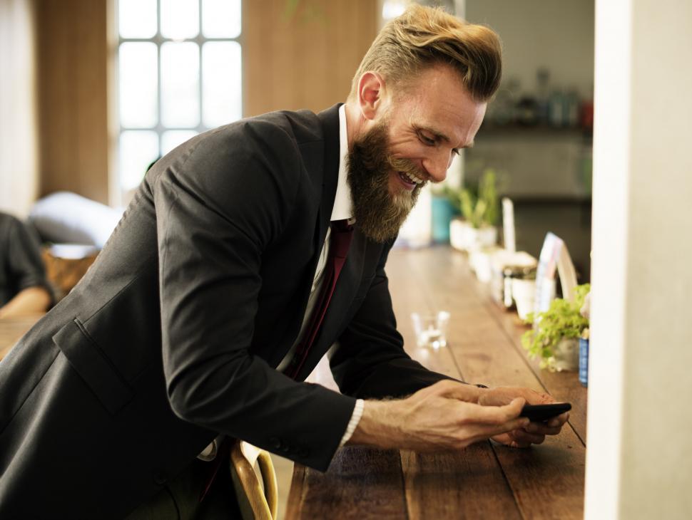 Free Image of A smiling bearded man looking at his mobile phone 