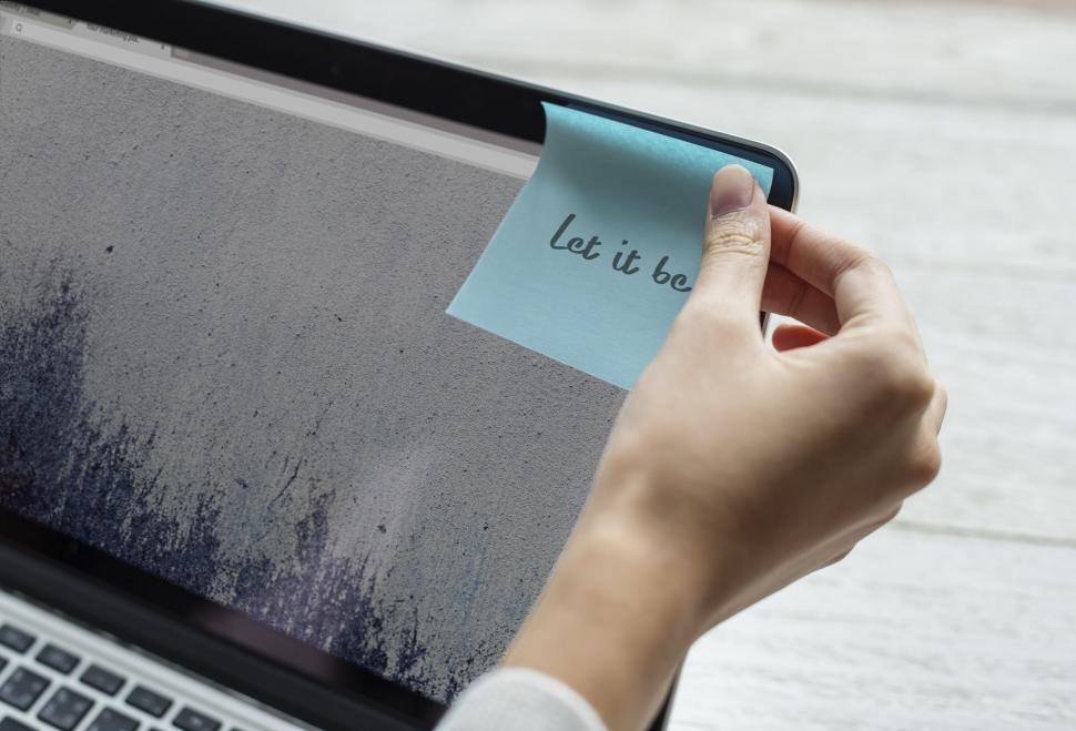 Free Image of A hand placing a sticky note on the edge of the laptop screen 