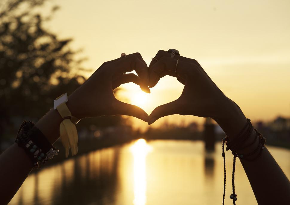 Free Image of A woman s hands making a heart shape against bright sunset 