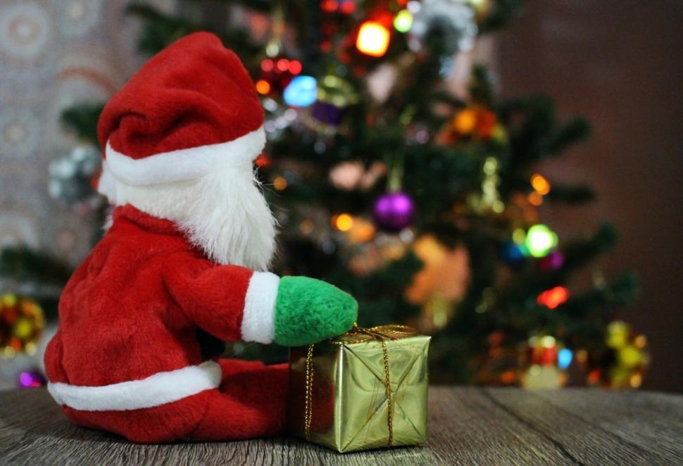 Free Image of Santa with present looks at Christmas Tree  