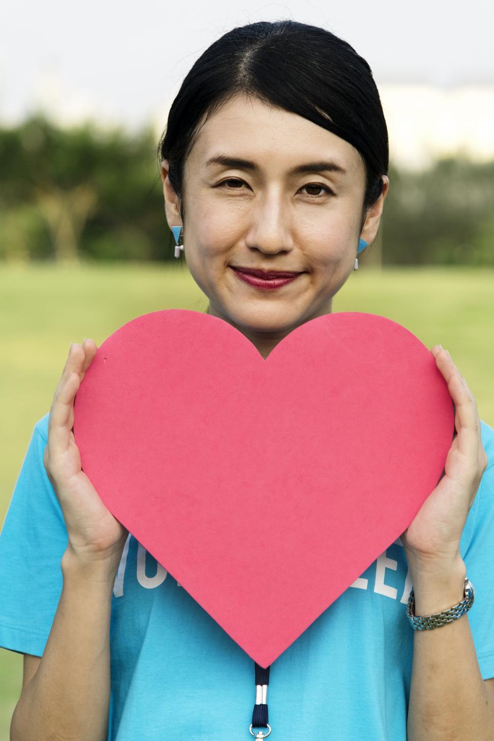 Free Image of A young Asian ethnicity woman posing with a red heart shaped cut out 