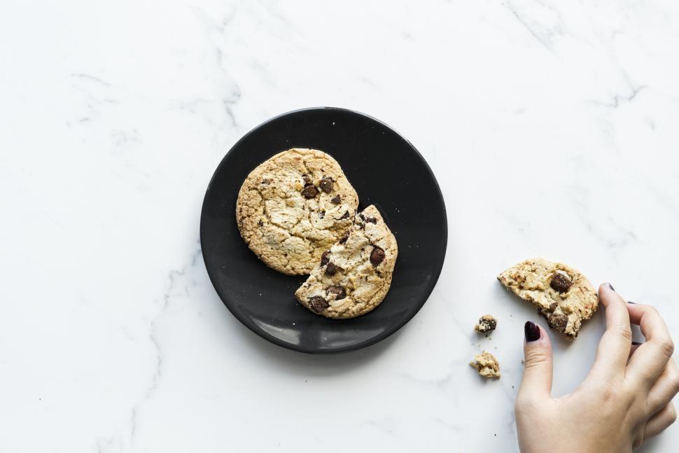 Free Image of Flat lay of a woman s hand picking up a piece of chocolate chip cookie 