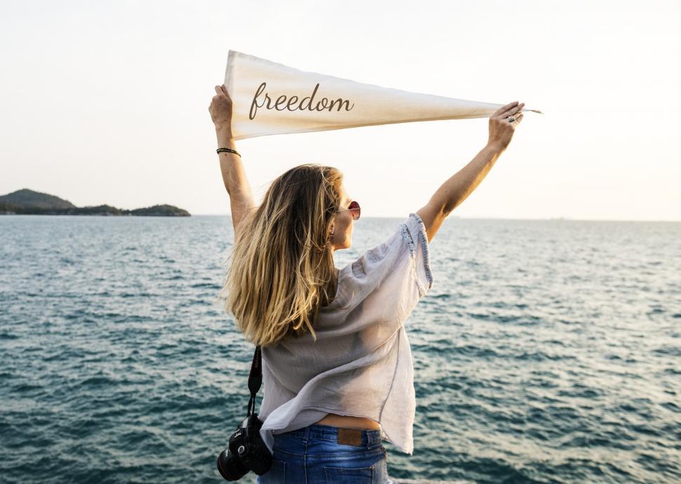 Free Image of A young Caucasian woman holding white flag high at a seashore 